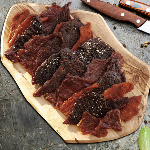 A photo of a platter of different exotic jerky on a wooden cutting board
