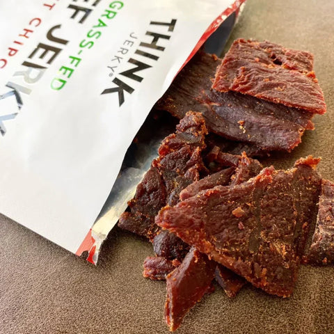 Think Jerky Sweet Chipotle – premium, tender slices of 100% grass-fed beef jerky with a bold, smoky-sweet chipotle flavor, spilling out of its packaging.