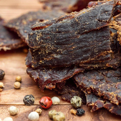 bison jerky slices with peppercorns on wooden surface