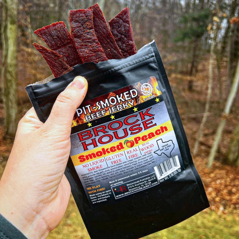 A photo of someone holding a bag of Brockhouse Smoked Peach beef jerky with hearty strips of jerky sticking out of the top of the packaging