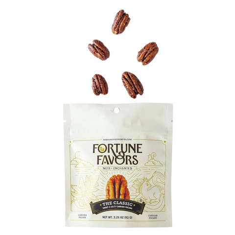 Bag of Fortune Favors 'The Classic' sweet & salty candied pecans with five glossy pecans floating above the package, showcasing their rich coating. The packaging features whimsical gold illustrations and the tagline 'Nuts Enchanted' on a white background.