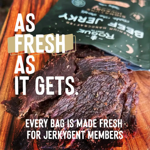 Close-up of fresh beef jerky on a wooden board with text overlay “As Fresh As It Gets. Every bag is made fresh for JerkyGent members.