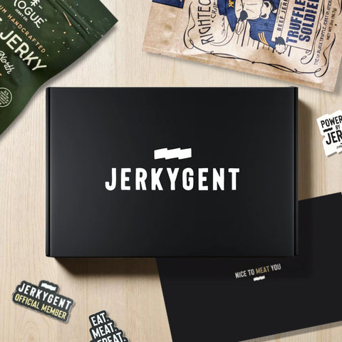 JerkyGent Beef Jerky Club Lifestyle Image showing the beef jerky subscription box, 2 bags of craft beef jerky, welcome to the club packet, and club stickers.