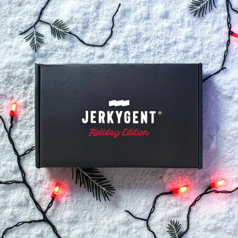 Black beef jerky gift box with 'Jerkygent' branding on a snowy background with Christmas lights and decorations.