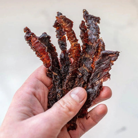 A close-up image of someone's hand holding some sugar-free beef jerky that is keto friendly