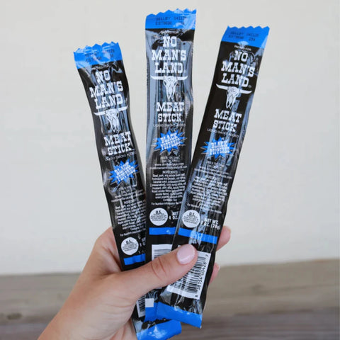 Hand holding three No Man’s Land Black Peppered Meat Sticks, 1 oz each, wrapped in black and blue packaging.