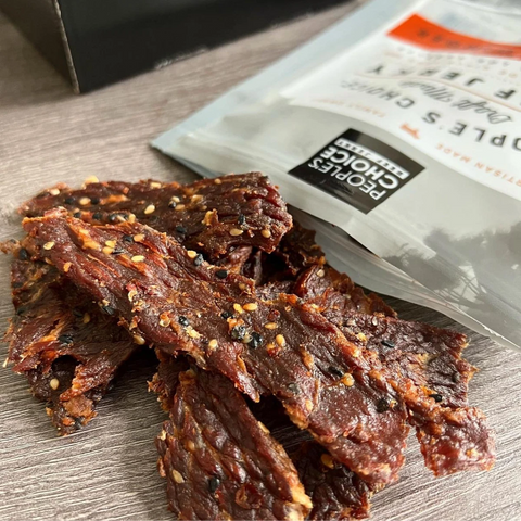 A close-up of People's Choice Garlic Ginger beef jerky coming out of the packaging to showcase the infusion of seeds and spices