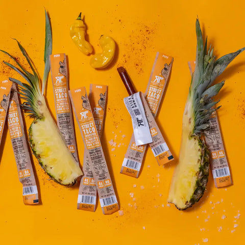 Righteous Felon Street Taco Beef Pork Sticks on an orange canvas surrounded by fresh pineapple