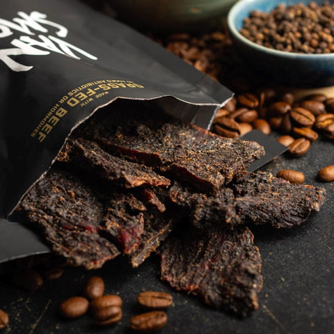 Van Smokey Breakfast In Bed Coffee and Pepper flavored beef jerky spilling out onto a table with coffee beans in the background.