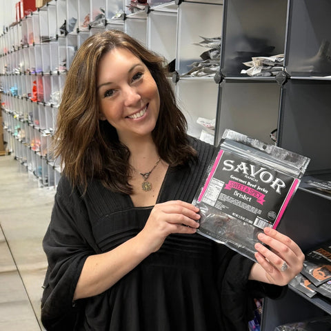 Beth from the JerkyGent team holding a bag of Savor Ranch Sweet & Spicy Brisket jerky, smiling in the fulfillment area.