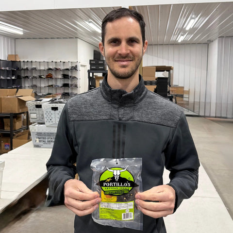 Chris holding a pack of Portillo’s Jalapeño Artisan Jerky in the JerkyGent warehouse, standing in front of shipping tables and shelves.