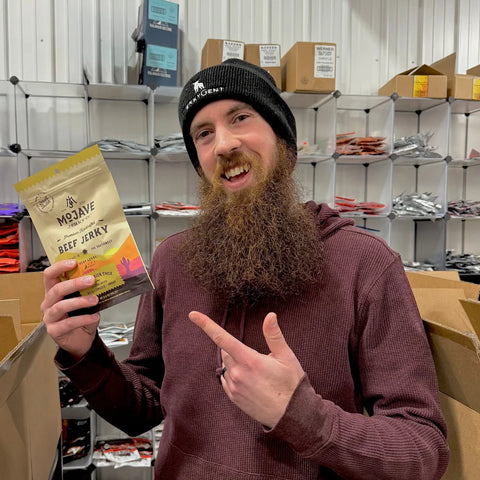 Taylor from the JerkyGent team smiling and pointing at his pick — Mojave Jerky Co.’s Hatch Green Chile jerky — in the packing area.