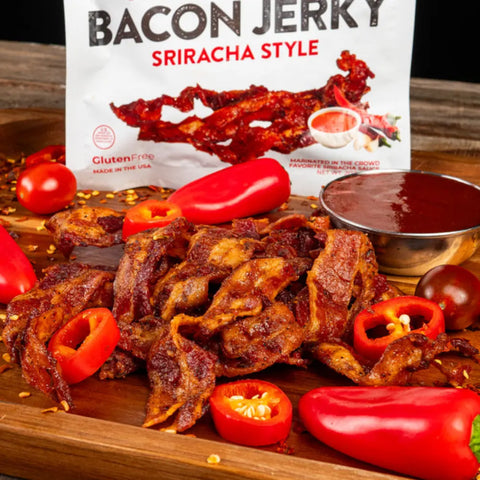 Wicked Cutz Sriracha Style Bacon Jerky surrounded by fresh red chili peppers and a bowl of sriracha sauce, placed in front of branded packaging.