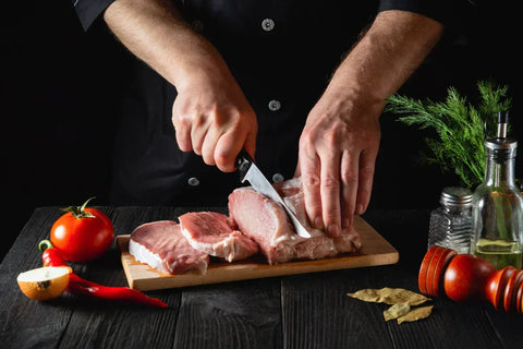 A photo of someone cutting raw meat into slices surrounded by fresh vegetables and other ingredients