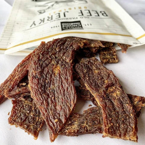 A pile of sugar-free beef jerky spilling out of a bag onto a wooden table, showcasing a delicious and guilt-free keto snack option from JerkyGent.