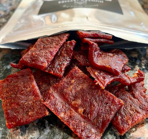 A bag of teriyaki beef jerky on a table showcasing the marbling of the meat and teriyaki glaze coating the beef jerky.