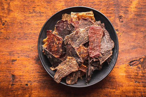 Crunchy beef jerky slices in a black bowl on a rustic wooden table