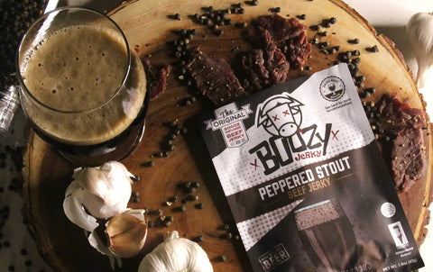 Peppered Stout Infused Beef Jerky next to a full glass of craft beer with beef jerky spread out over the table.