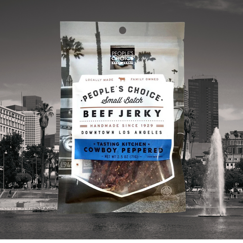 Bag of People’s Choice Small Batch Beef Jerky, Tasting Kitchen Cowboy Peppered flavor, handmade since 1929 in downtown Los Angeles, displayed with city skyline background.