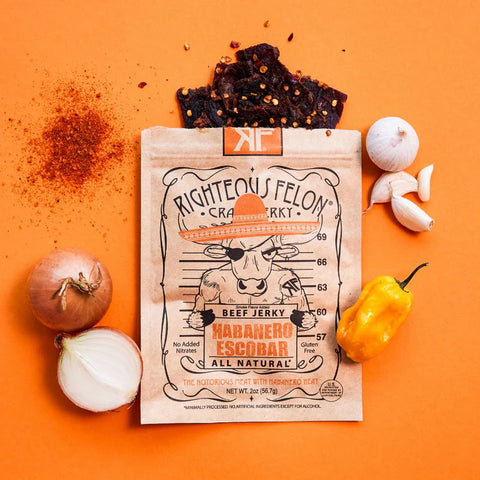 Righteous Felon Habanero Escobar beef jerky package on an orange background with spices and peppers.