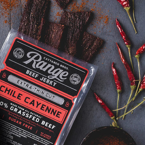 A close-up photo of Chile Cayenne extra-thin cut beef jerky by Cattaneo Bros. along with a spread of peppers and cayenne seasoning