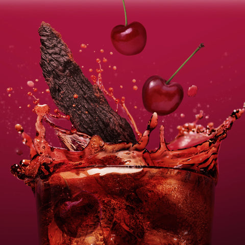 Glass of dark liquid with cherries and chocolate pieces against a red background