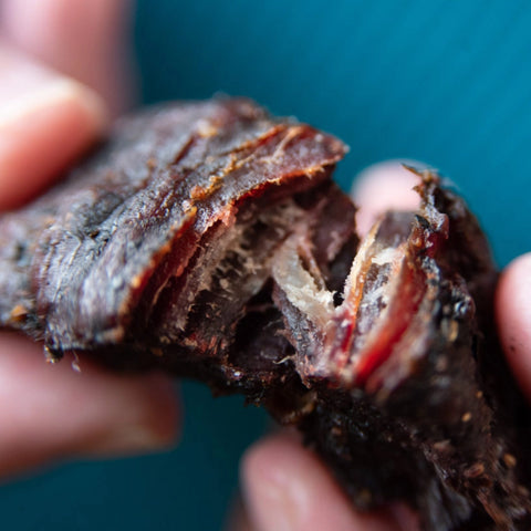 A super close-up photo of someone breaking open a piece of beef jerky to test the doneness of the jerky