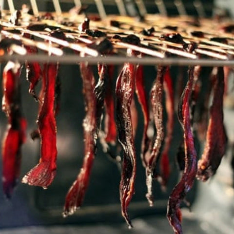 A photo of multiple pieces of beef jerky that are all hanging to dry