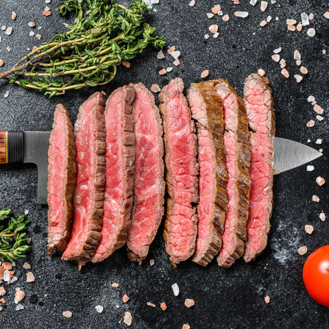 A close-up photo of perfectly cooked thin-cut flank steak surrounded by seasonings and spices 