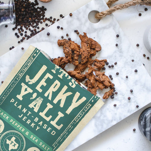 It's Jerky Yall opened with vegan jerky on a table surrounded by black pepper.