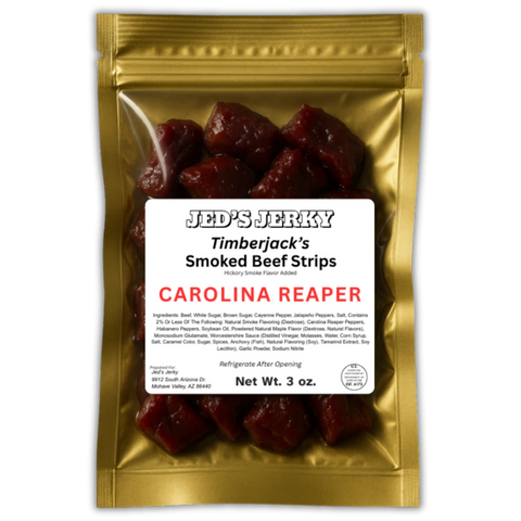 Jed’s Jerky “Timberjack’s Smoked Beef Strips” in the Carolina Reaper flavor. The front features a horizontal white label with bold black retro lettering for “Jed’s Jerky,” followed by “Timberjack’s Smoked Beef Strips” and “Carolina Reaper” in bright red. The label includes a full ingredients list, net weight, and storage instructions. Through the clear window, thick, juicy, hand-cut beef chunks are visible, showcasing a rich, dark reddish-brown color.
