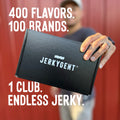 Person holding a beef jerky subscription box with 'Jerkygent' branding against a red curtain background.