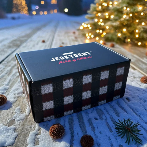 Jerky Gent Holiday Edition box with plaid design on a snowy surface with Christmas tree in background