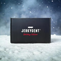 Black JerkyGent Holiday Edition gift box sitting on snowy ground with falling snow and frosty winter background.