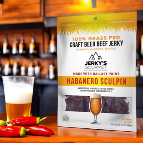 An image of Jerky's Gourmet Habanero Sculpin on a counter top inside of a bar next to a glass of beer and several peppers