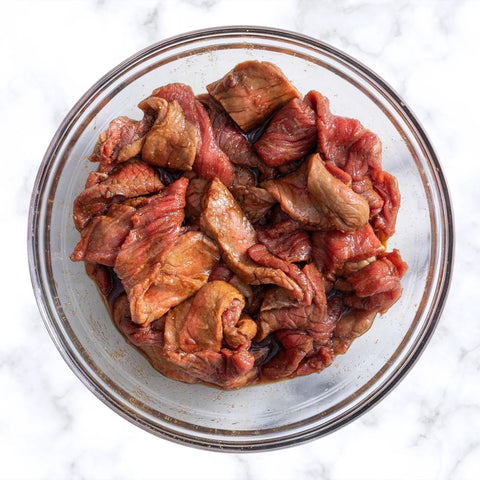 A top-view of a bowl of chopped meat that is marinating in liquids and seasonings