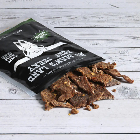 No Man’s Land Dill Pickle Beef Jerky pieces spilling from open bag onto wooden surface.