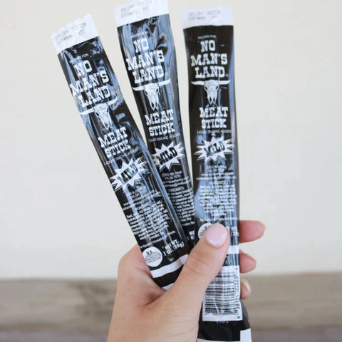 Hand holding three No Man’s Land Mild Meat Sticks, 1 oz each.