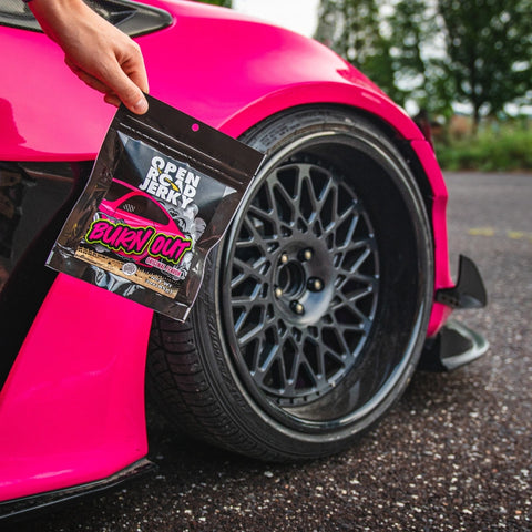 Open Road Jerky Original Burn Out Beef Jerky held in front of pink muscle car