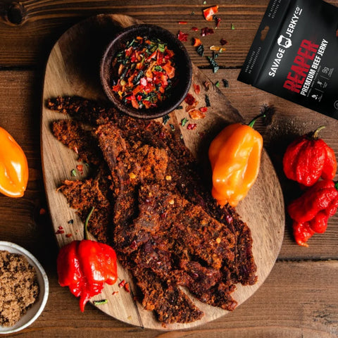 A top-view image of Reaper beef jerky by Savage Jerky Co. along with a spread of various peppers and spices