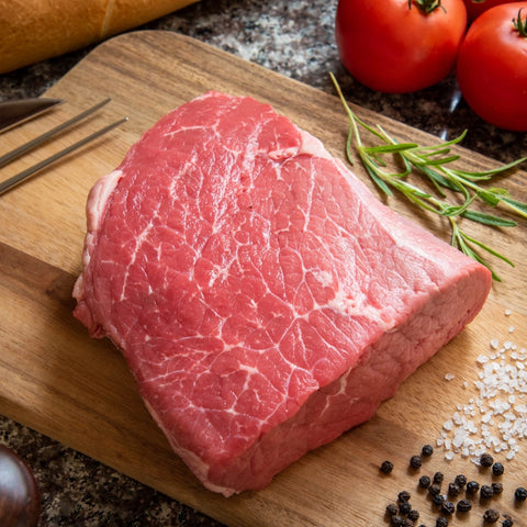 Raw top round steak on a cutting board with some marbling visible surrounded by other cooking ingredients