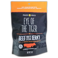 Front of a “Praise the Graze – Eye of the Tiger” Beef Ribeye Steak Jerky bag. The design features bold white and orange text on a black matte background. The top reads “100% Grass Fed Beef with Redmond’s Unrefined Sea Salt…That’s It!” Below, the name “Eye of the Tiger” is prominently displayed with “Beef Ribeye Steak Jerky” underneath. It is labeled as a product of Arizona Grass Raised Beef Co., with a red cow silhouette and mountain range graphics at the bottom. The net weight is 2.5 oz.